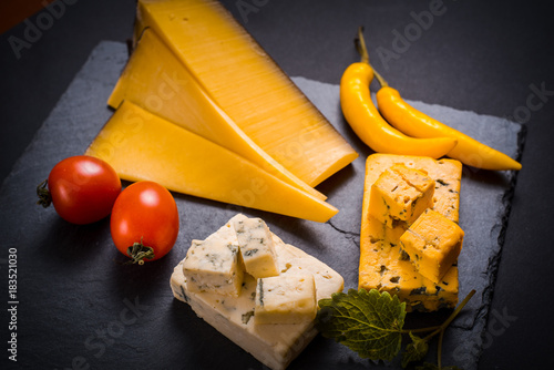 Cheese with mold, cherry tomatoes, basil and melissa greens, red hot pepper on a stone tray on a dark gray background photo