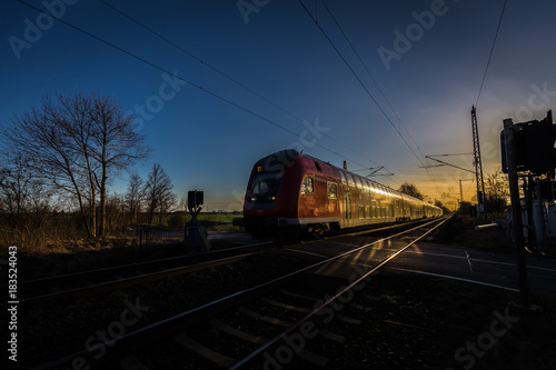 Fotografie Beautiful blue and yellow sunset on level crossing, double track with passing tr
