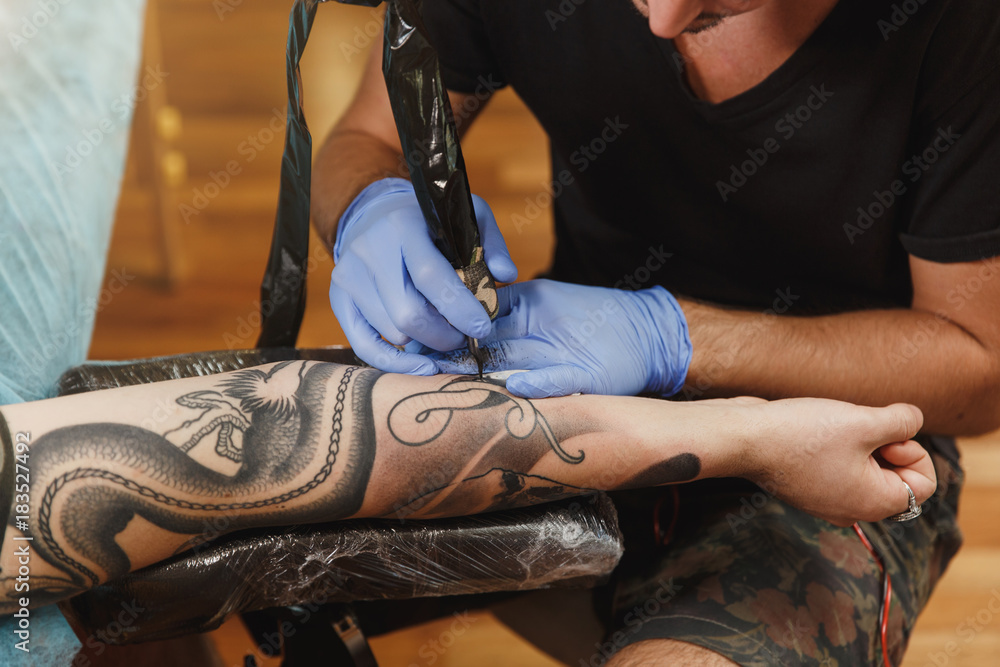 Close up of professional tattooer artist doing picture on hand of man by machine black ink Close up of professional tattooer artist doing picture on hand of man by machine black ink