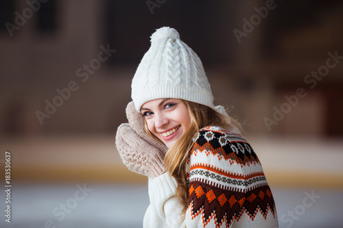 Autumn, Winter portrait: Young smiling woman dressed in a warm woolen cardigan, gloves and hat posing outside.