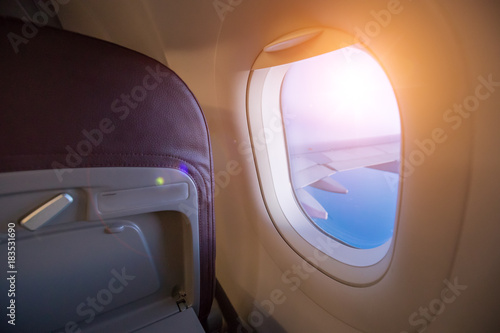 View from passenger's seat in airplane flying above clouds in dramatic sunset light.