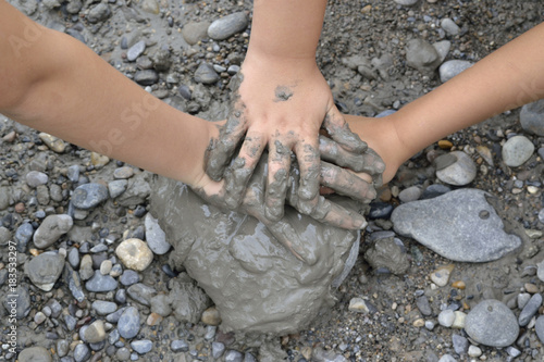 Manos de niño, una sobre otra, con barro, sobre una piedra.