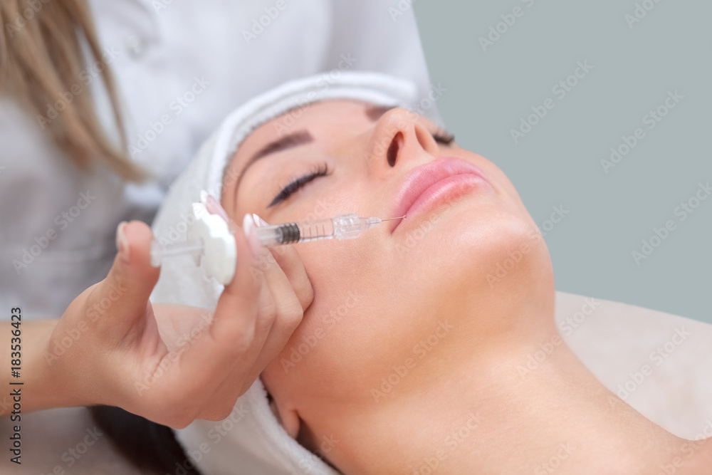 The doctor cosmetologist makes the Botulinotoxin injection procedure for tightening and smoothing wrinkles on the face skin of a beautiful, young woman in a beauty salon.Cosmetology skin care.