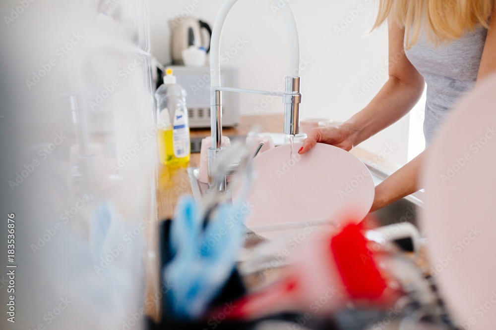 Young woman washing dishes in sink Young woman washing dishes in sink