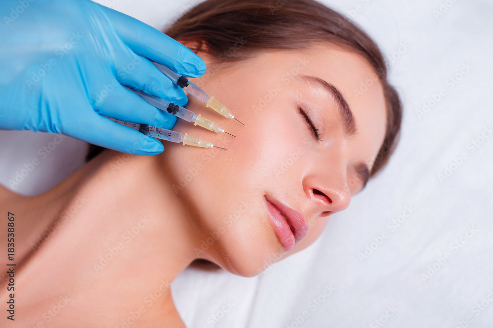 Beauty Injection. Closeup Of Doctor Hands With Syringes Near Female Face. Portrait Of Beautiful Woman Receiving Facial Skin Lifting Treatment.