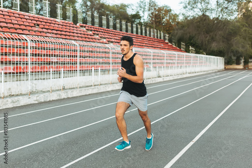 Young athletic man running on the stadium in the morning