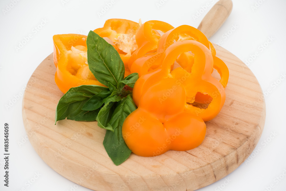 Freshness composition with orange bell pepper and basil on cutting board isolated on white background