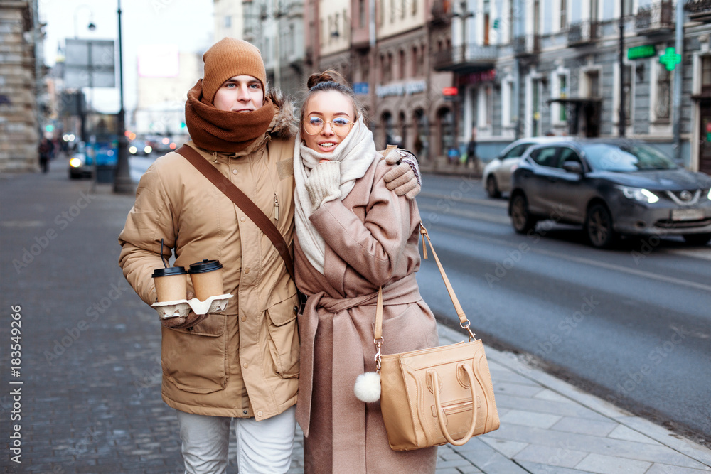 Beautiful young couple in love are walking on the street in cold winter with coffee and have fun together
