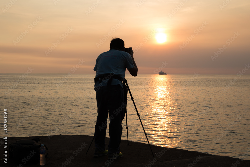 Silhouette photographer taking photo of ocean at and sunset