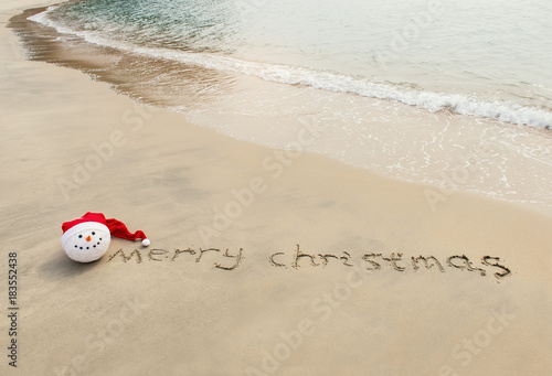 Merry Christmas written on tropical beach white sand with xmas snowman