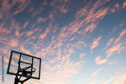 Silhouette of outdoor basketball goal with clear backboard and sunset in the background