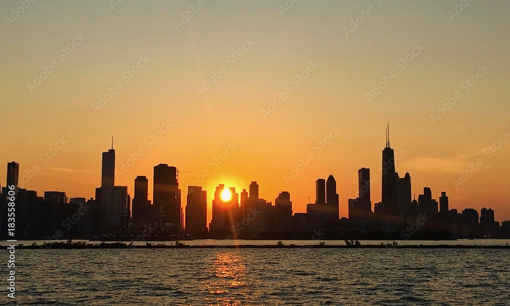 Sunset over Chicago skyline with ball of sunlight peeking through buildings