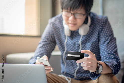 Young Asian man half face holding credit card and using smartphone for online shopping in his workspace, urban lifestyle concept