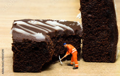miniture people worker digging into the chocolate cake