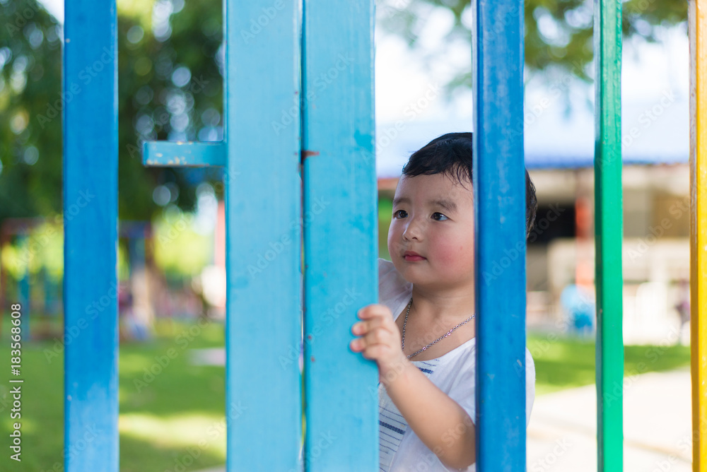Obraz premium Smile Asian kid behind the colorful fence at playground in summer. shallow DOF.