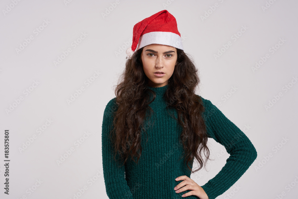 brunette woman holding her hand at the waist, green dress, Christmas hat, light background, new year brunette woman holding her hand at the waist, green dress, Christmas hat, light background, new year