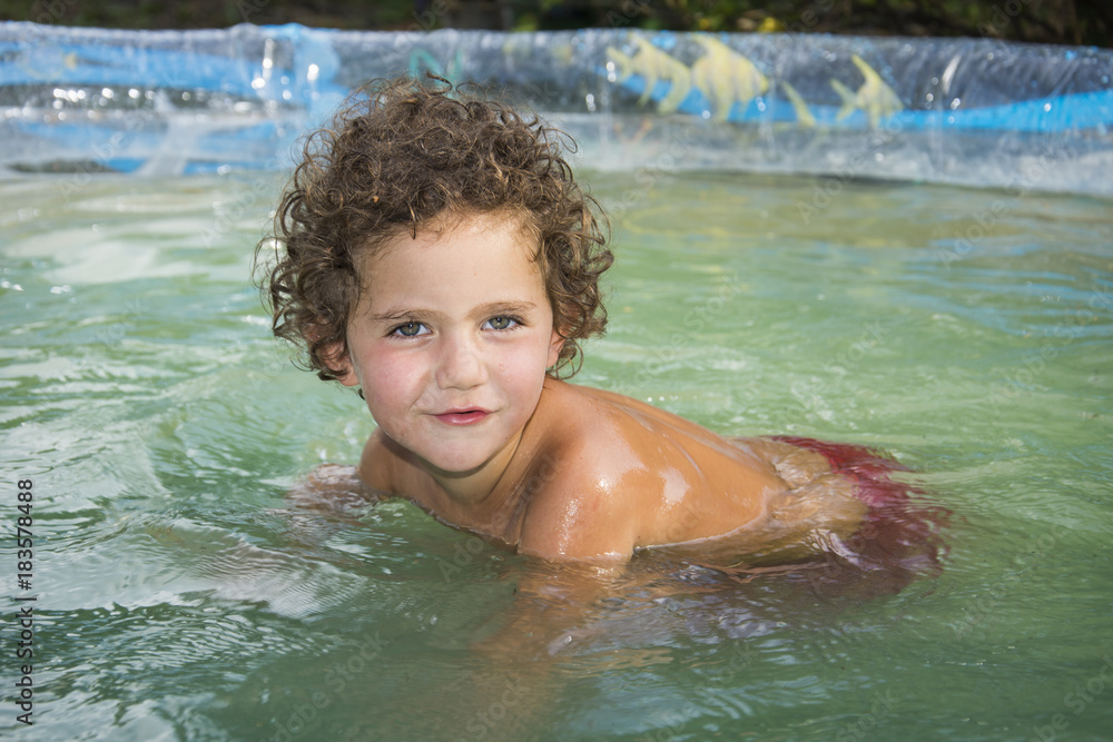 In the summer in the courtyard in the pool sits a small handsome wet girl.