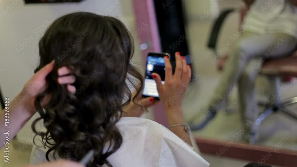 The girl does a hairdress at the hairdresser and looks through her iPhone.close up. stylist makes woman's hairdress in an art salon. The girl does a hairdress at the hairdresser and looks through her iPhone.close up. stylist makes woman's hairdress in an art salon.
