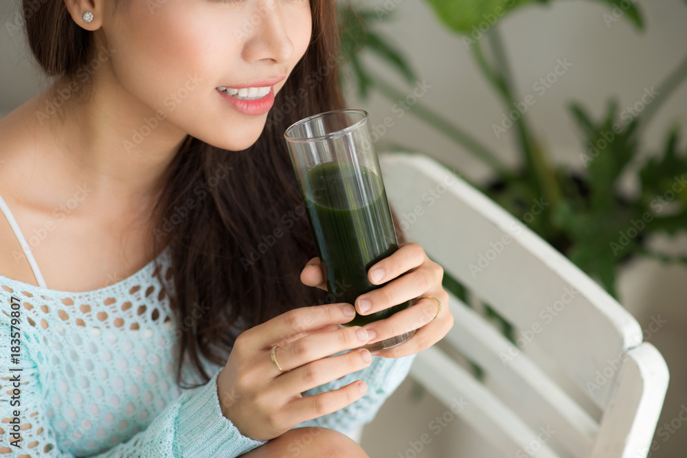 Smiling young asian woman drinking green fresh vegetable juice or smoothie from glass at home Smiling young asian woman drinking green fresh vegetable juice or smoothie from glass at home