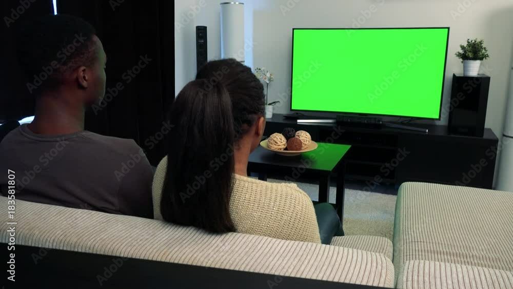 Young black couple watch television in living room and then smile to camera Young black couple watch television in living room and then smile to camera
