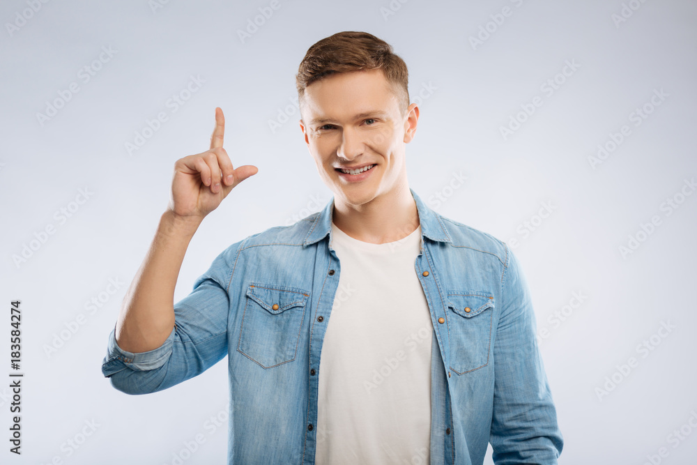 Having plan. Handsome male keeping smile on his face and raising forefinger while looking straight at camera Having plan. Handsome male keeping smile on his face and raising forefinger while looking straight at camera