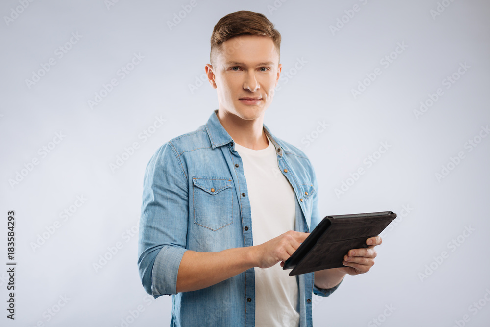 Going to work. Confident young man expressing positivity and using tablet, standing over grey background Going to work. Confident young man expressing positivity and using tablet, standing over grey background