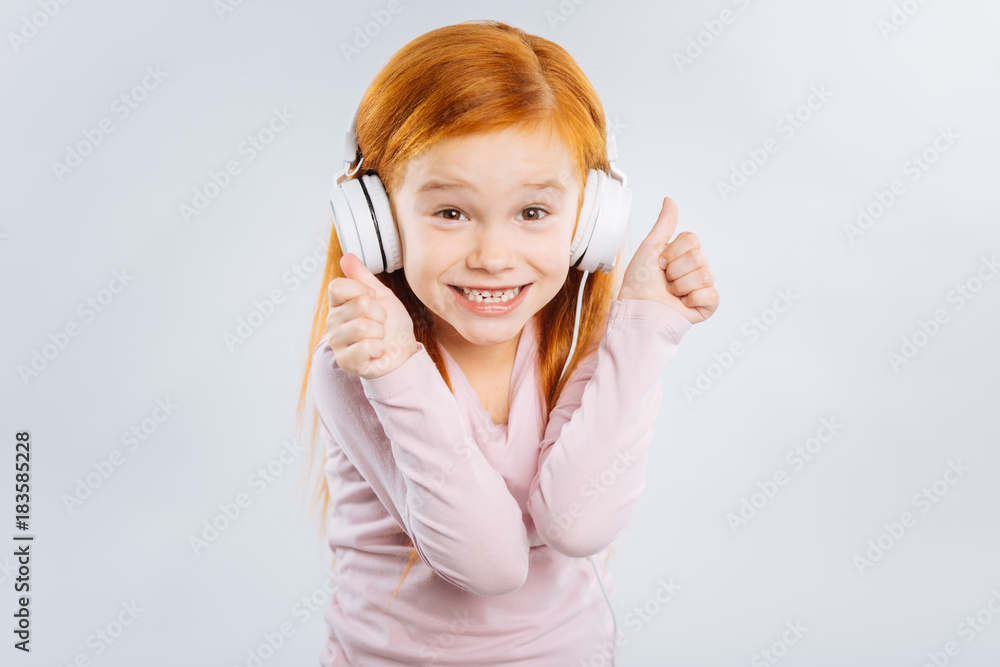The best. Charming kid expressing positivity, wearing headphones while standing isolate on grey background The best. Charming kid expressing positivity, wearing headphones while standing isolate on grey background