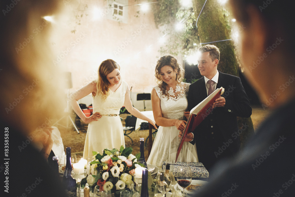 Φωτογραφία Laughing wedding couple stands at the dinner table and looks at the photoalbum