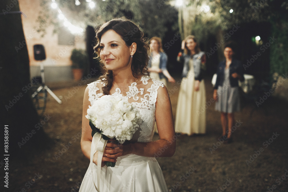 Bride stands with wedding bouquet before their friends ready to throw it