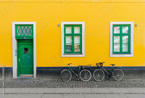 Old style bicycles parked against yellow wall.