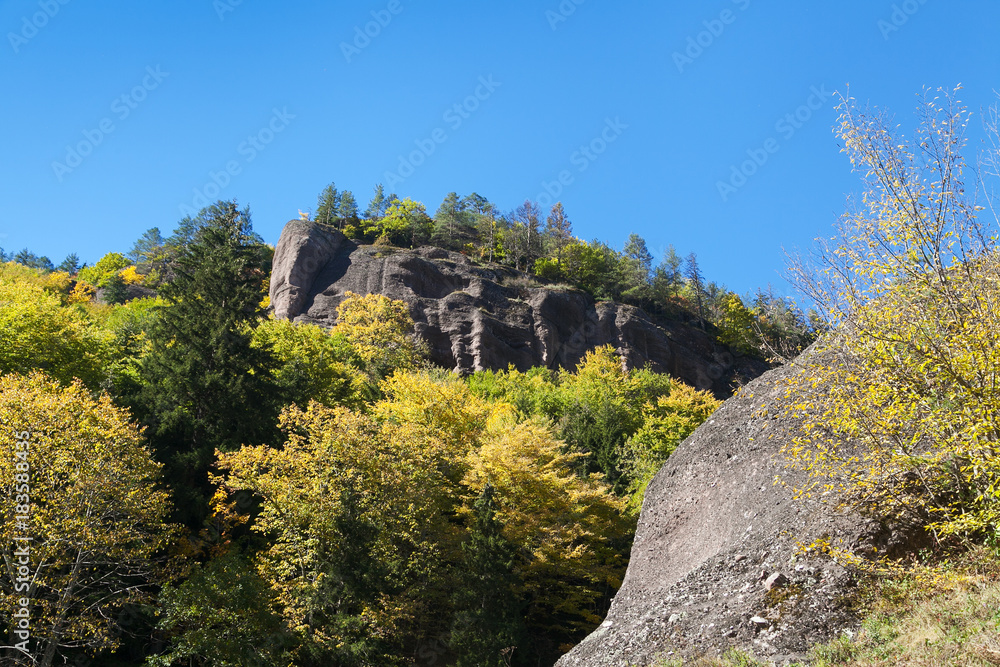 At the foot of a granite hill with trees on top and blue sky