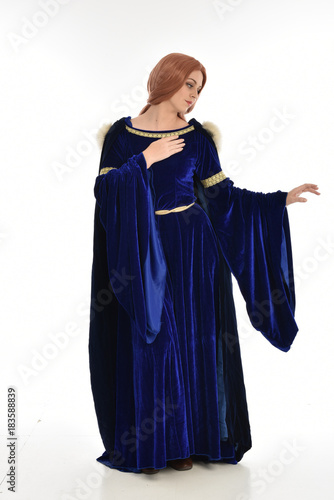 full length portrait of girl wearing long blue velvet gown and fur lined cloak, standing pose on white background.