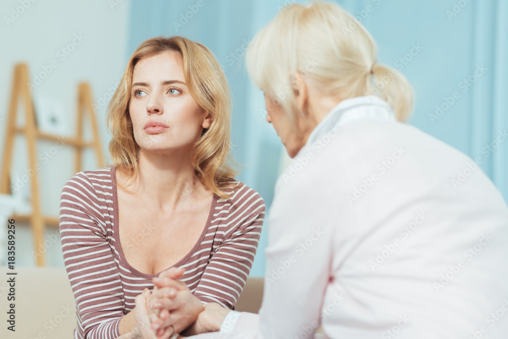 Upset woman. Young exhausted sad woman sitting and looking into the distance while her caring attentive grandmother touching her hands and helping to solve the problem Upset woman. Young exhausted sad woman sitting and looking into the distance while her caring attentive grandmother touching her hands and helping to solve the problem