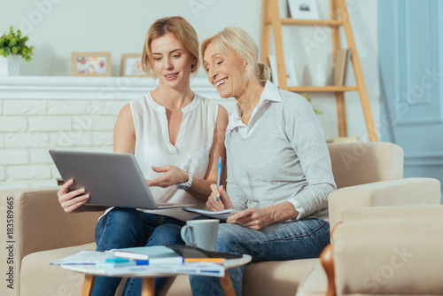 Good results. Responsible clever aged woman feeling happy while looking at the screen of a modern laptop and having an important conversation with her experienced reliable financial advisor