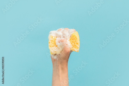 cropped view of hand holding washing sponge with foam, isolated on blue photo