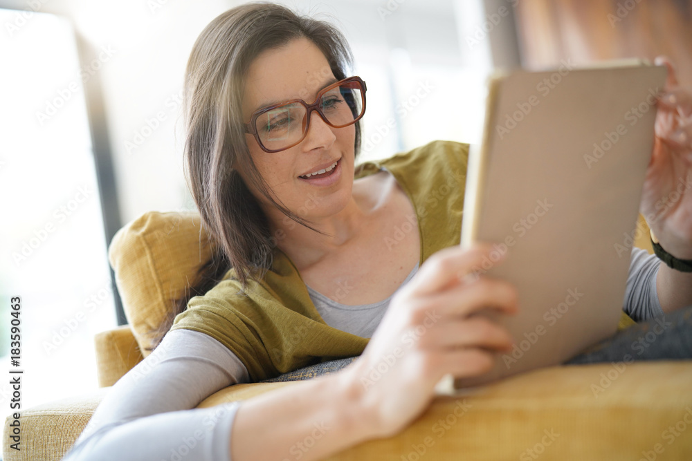 Brunette woman with eyeglasses using tablet, sitting on sofa Brunette woman with eyeglasses using tablet, sitting on sofa