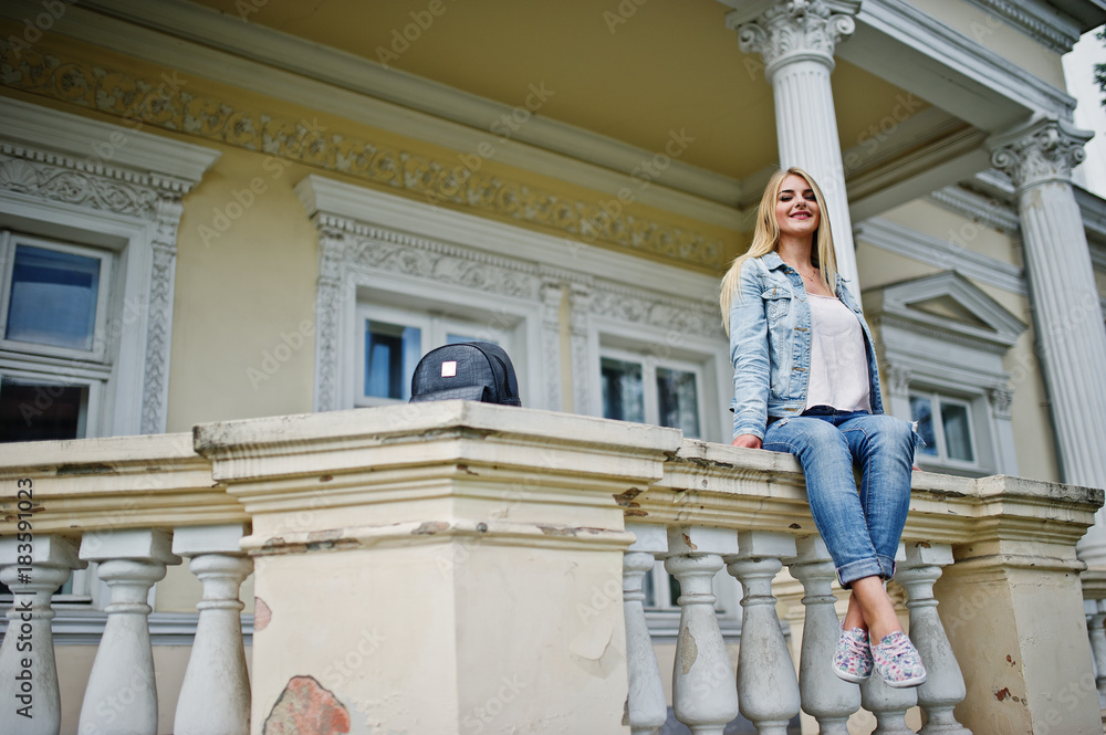 Blonde girl wear on jeans with backpack posed against vintage house.