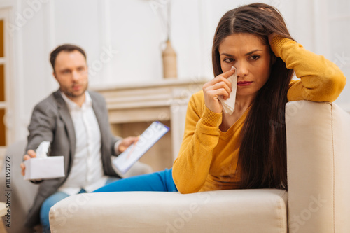 Do not cry. Fabulous upset female patient sitting on the couch looking aside while doctor proposing her  tissue 
