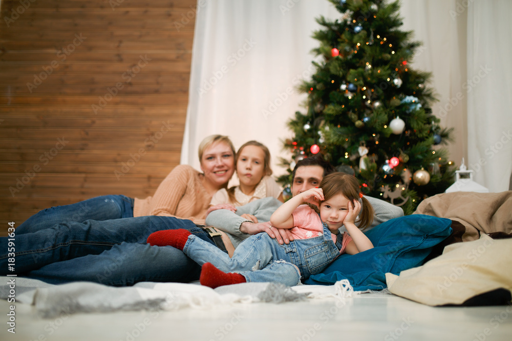 Photo of happy family with two daughters lying on floor against backdrop of New Year's decorations