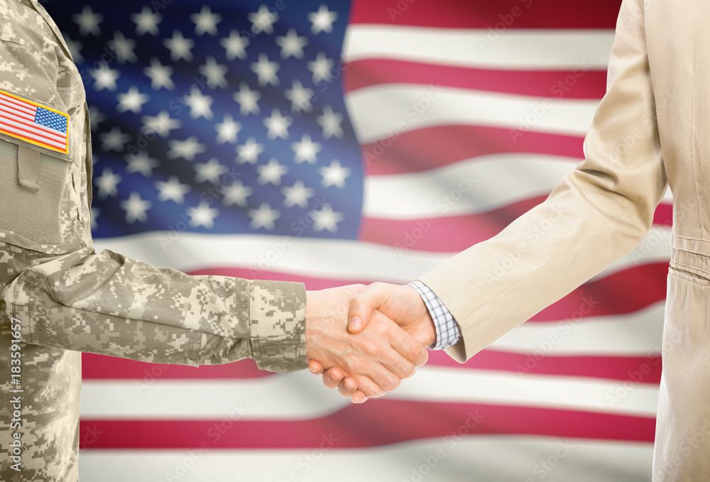 Fototapeta premium USA military man in uniform and civil man in suit shaking hands with adequate national flag on background - United States of America