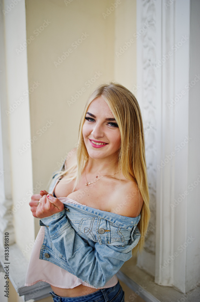 Blonde girl wear on jeans posed against old house.