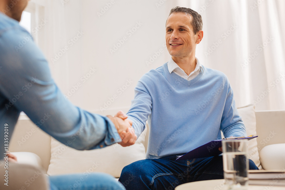 Pleasant acquaintance. Attractive handsome kind man smiling sitting on the sofa and shaking hands Pleasant acquaintance. Attractive handsome kind man smiling sitting on the sofa and shaking hands