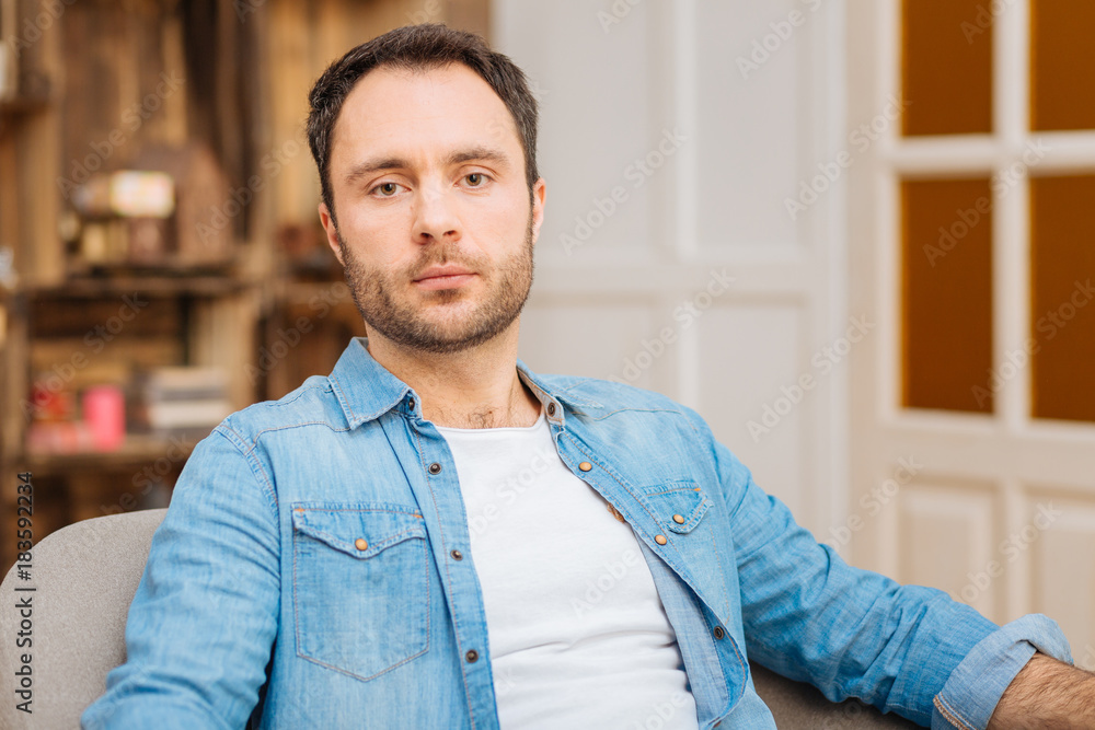 Disappointing truth. Upset earnest young man sitting staring at the camera while posing on the blurred background Disappointing truth. Upset earnest young man sitting staring at the camera while posing on the blurred background