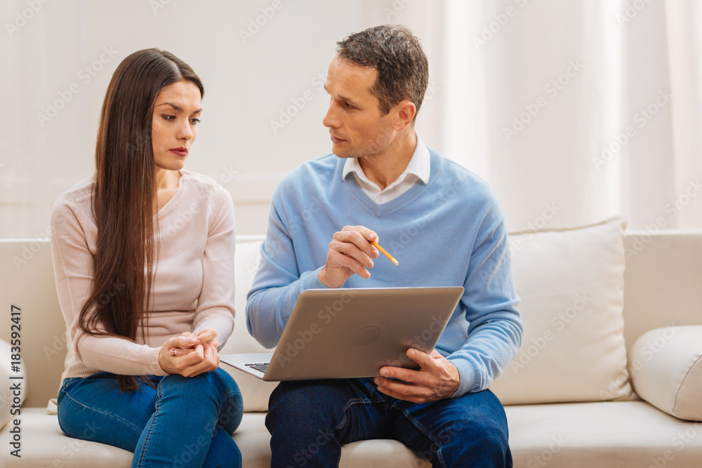 Vacation coming. Loving serious thoughtful couple talking about vacation while he holding laptop and examining her reaction Vacation coming. Loving serious thoughtful couple talking about vacation while he holding laptop and examining her reaction