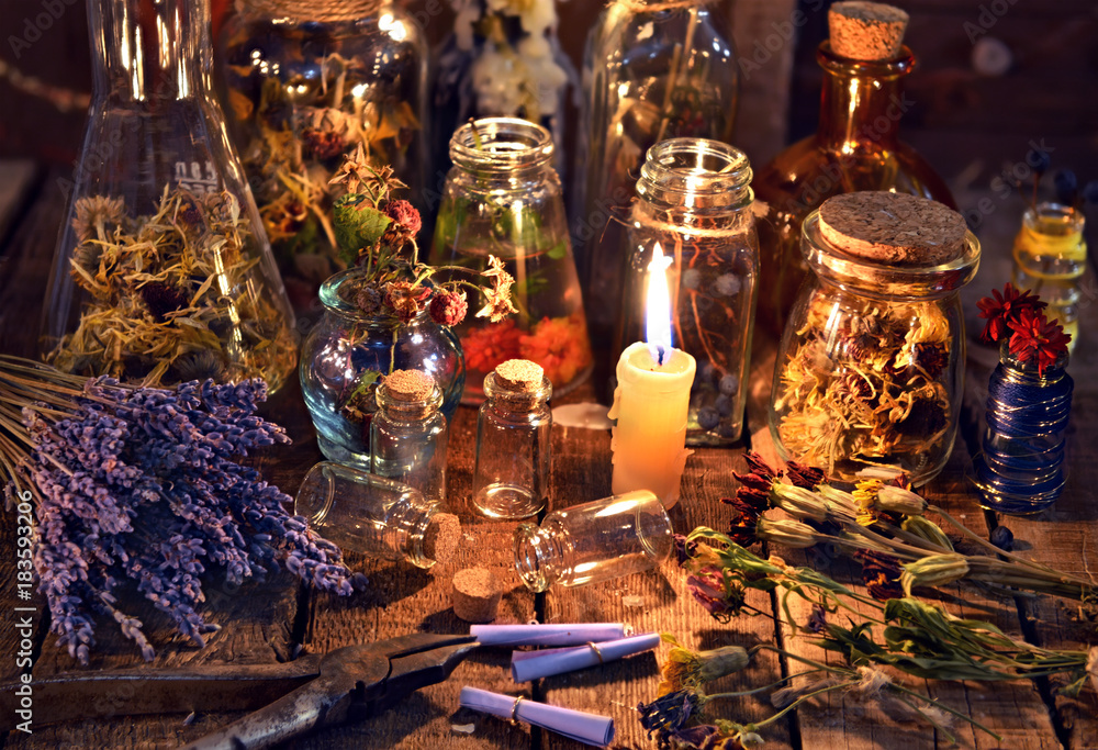 Bottles with herbs, lavender flowers, paper scrolls and magic objects on witch table. Occult, esoteric, divination and wicca concept. Mystic, old apothecary and vintage background