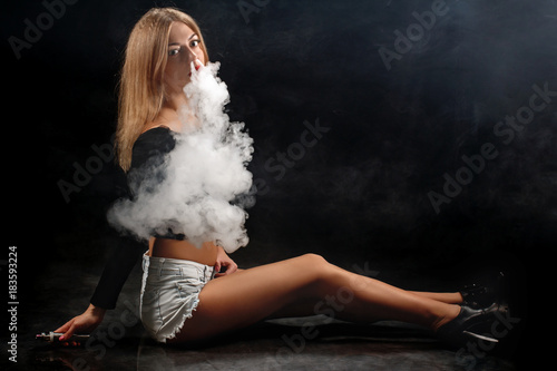 Beautiful girl vaping from e-cigarette on a black background