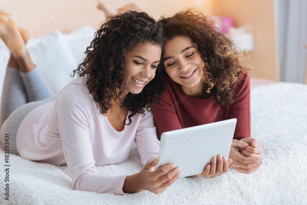 Time to relax. Extremely happy female friends relaxing on a bed and smiling with joy while spending some leisure time with a tablet computer. Time to relax. Extremely happy female friends relaxing on a bed and smiling with joy while spending some leisure time with a tablet computer.