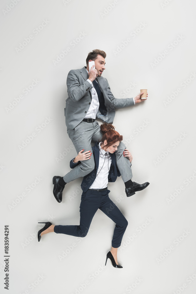 overhead view of businesswoman carrying businessman that talking on smrtphone isolated on grey