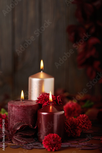 Three candles of crimson and pink color on a dark background with cones  leaves and daisies.