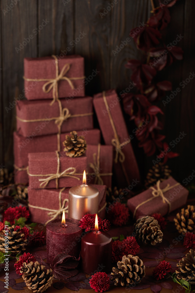 Three candles of crimson and pink color on the background of gift boxes with cones, leaves and daisies. Three candles of crimson and pink color on the background of gift boxes with cones, leaves and daisies.
